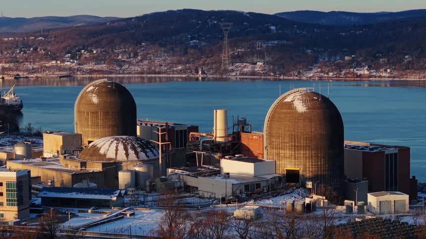 Aerial view of a nuclear power plant with snow-covered reactor domes situated on a riverbank during a golden winter sunset