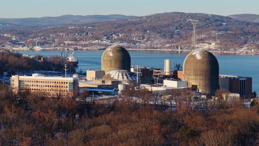 An aerial view slowly zooms in on a nuclear power plant during a bright winter day on a wide river