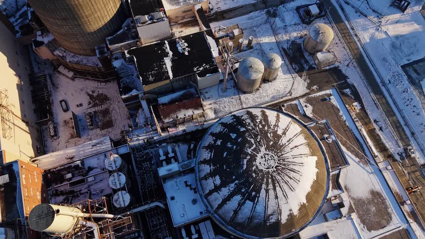 A slow top-down aerial view of a large, snow-covered industrial power plant complex on a cold winter day