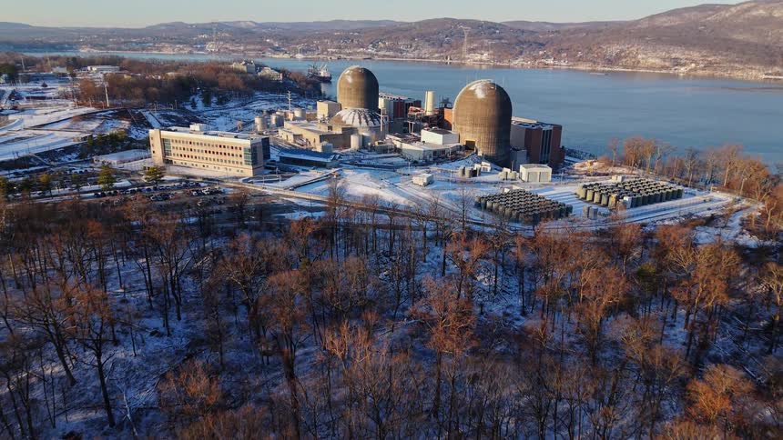 An aerial view pulls back from the Indian Point nuclear power plant, revealing its location on the snowy banks of the Hudson River during a winter sunrise