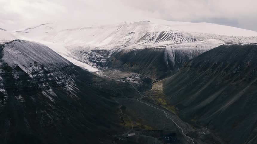 Dramatic aerial footage captures a stark and vast landscape where snow-covered peaks meet a dark, winding valley
