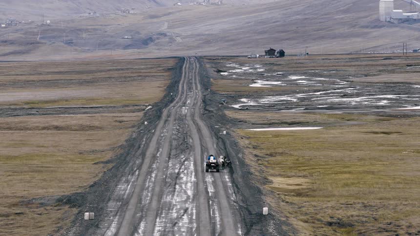 Two people and an ATV journey down a long, muddy road through a vast and desolate landscape