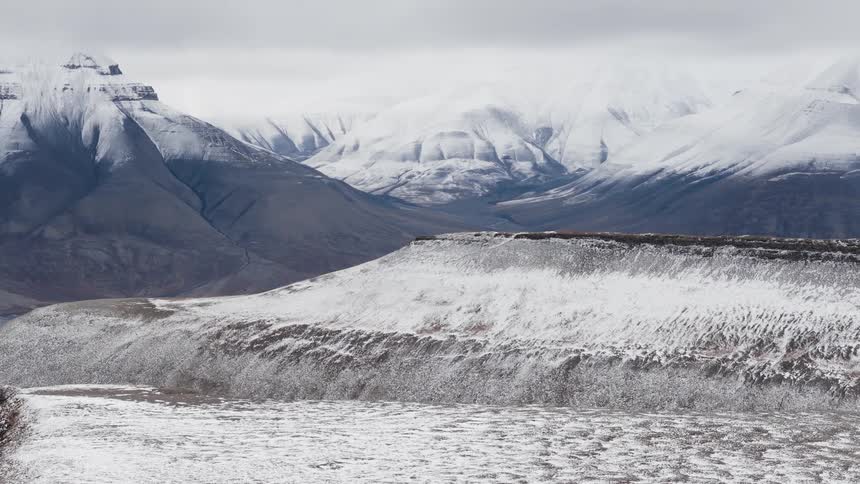 A slow zoom-out reveals a vast, desolate, and snow-covered mountain landscape under a cloudy sky