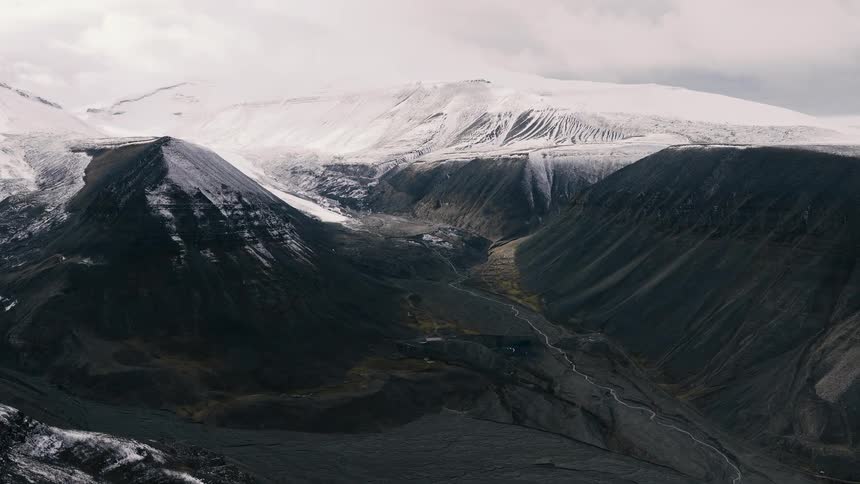 A slow, epic aerial dolly shot pulls back to reveal a vast, snow-covered mountain landscape with a deep, dark valley