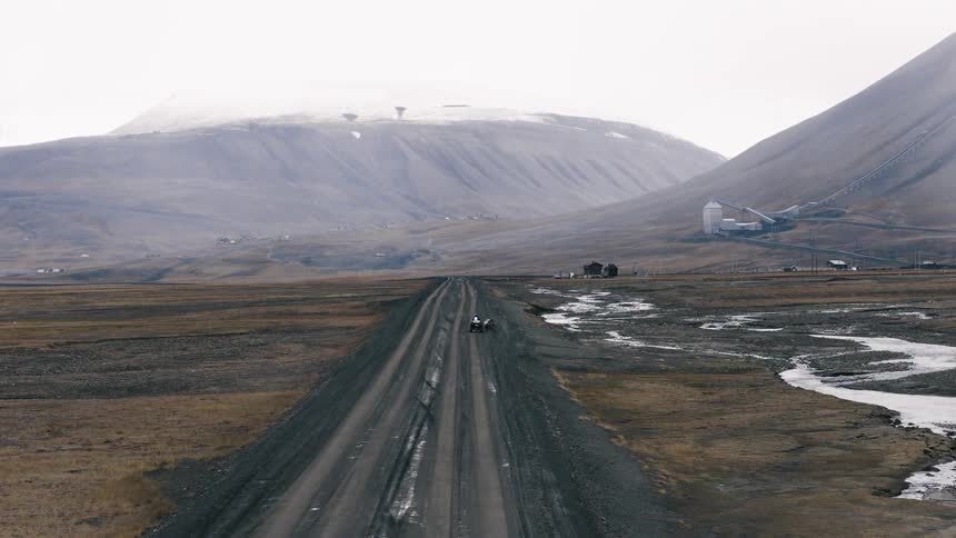 A horse-drawn buggy travels down a long, straight dirt road through a vast, desolate arctic landscape with mountains and industrial buildings in the distance