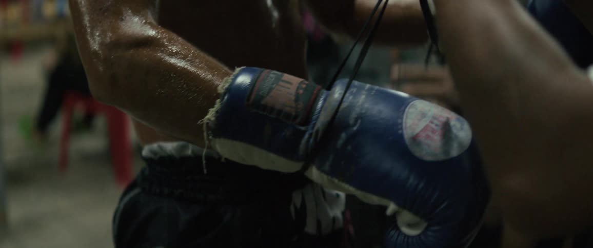 Intense slow-motion close-up of a sweaty boxer's coach lacing up his worn boxing gloves
