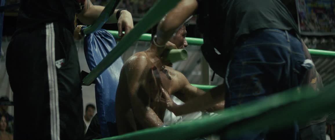 An exhausted Muay Thai boxer is massaged and doused with water in slow motion by his cornermen between rounds