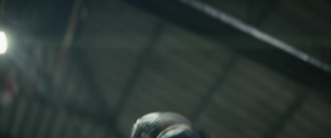 A dramatic slow-motion close-up of two men sparring in a dimly lit boxing ring