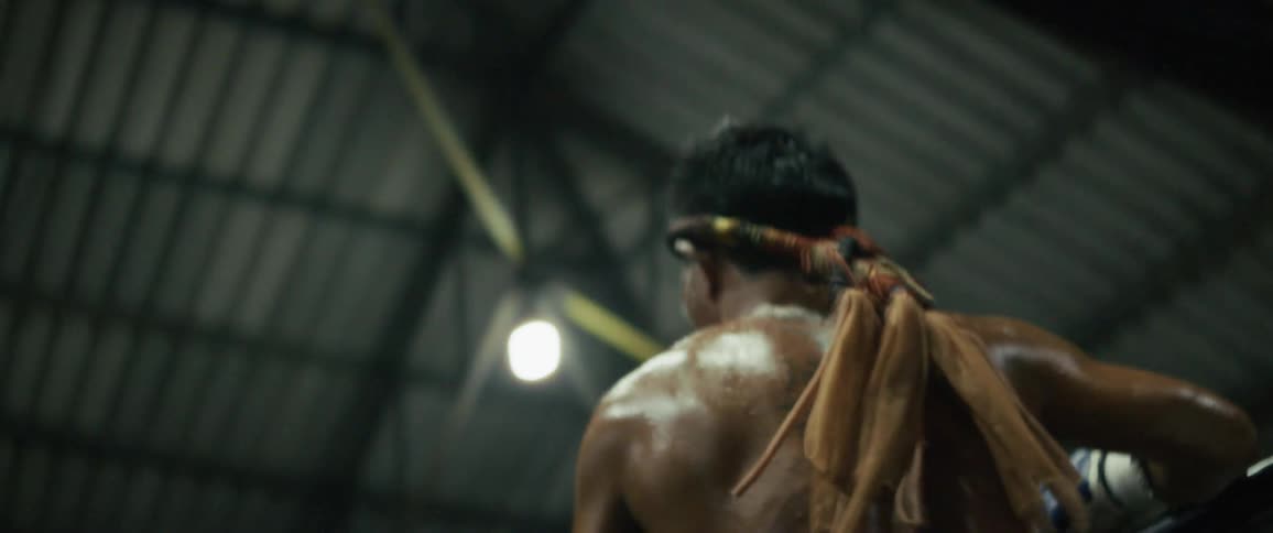 A tired and sweaty Muay Thai fighter takes a moment to rest on the ropes before turning to face his opponent in slow motion