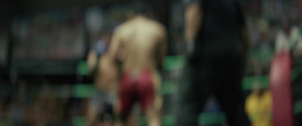 An out-of-focus, slow-motion view of two fighters in a boxing ring, with a referee visible in the foreground