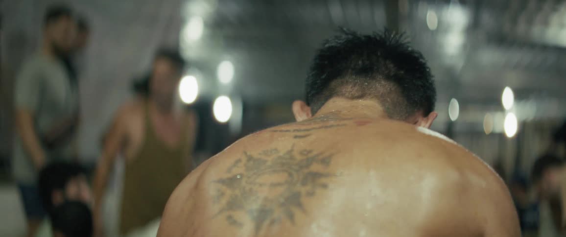 An intimate slow-motion close-up reveals the sweaty, bruised, and tattooed back of a male fighter in a boxing ring