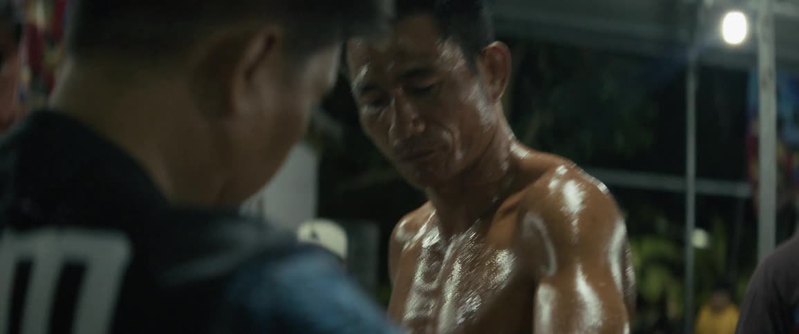 A muscular and sweaty Muay Thai fighter gets his hands wrapped by his trainer in slow motion before a big fight
