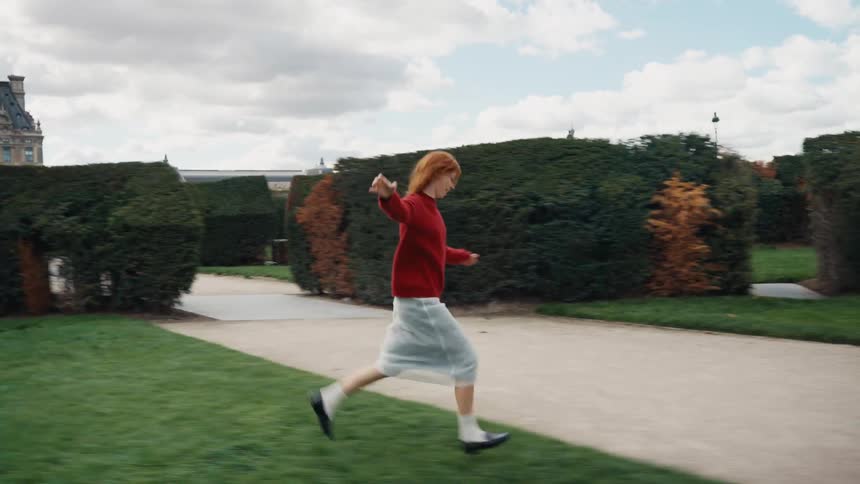 A joyful young woman with long red hair runs with carefree abandon through a beautiful park in slow motion