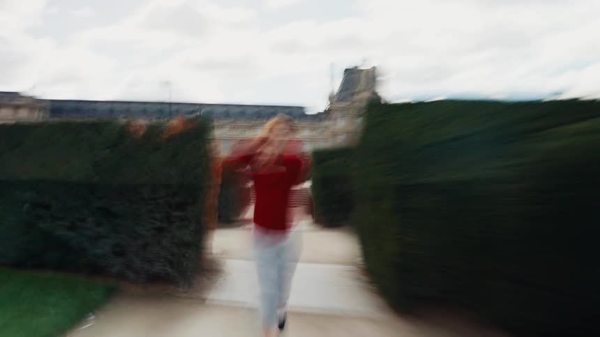 A stylized, dreamy shot shows a happy woman in a red sweater running playfully through a Parisian garden