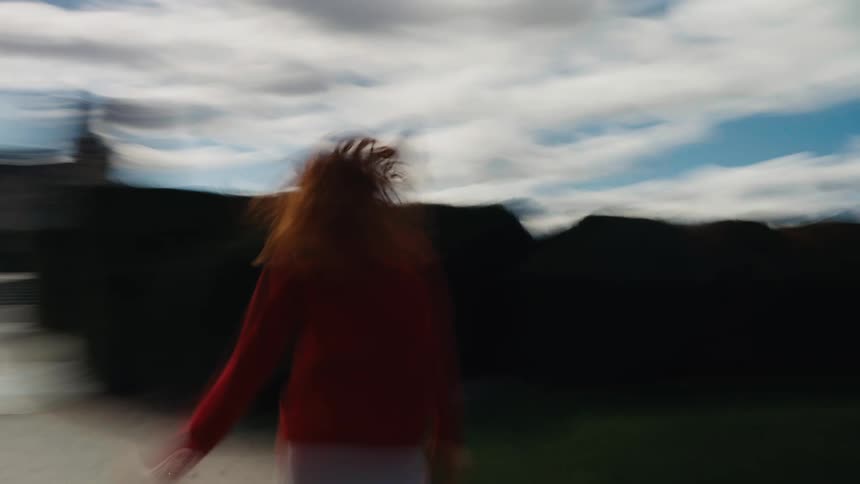Dreamy, motion-blurred footage of a redhead woman running through a formal garden towards a grand Parisian palace