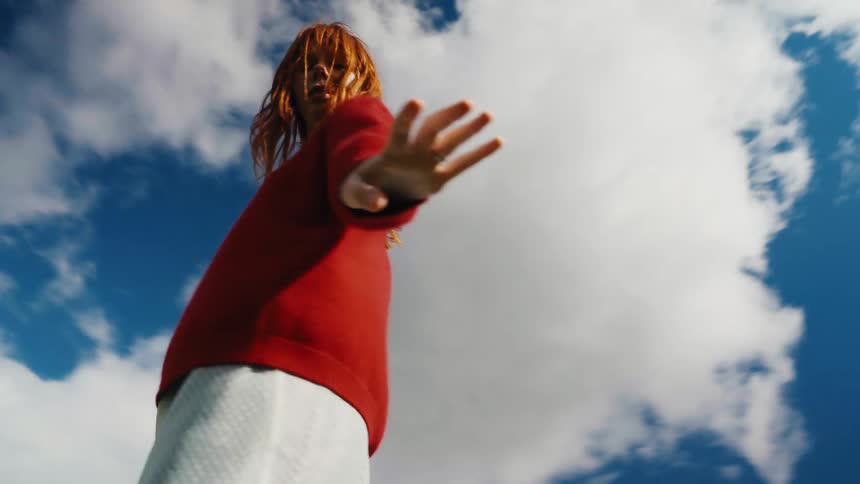 Low angle slow motion shot of a free-spirited woman with red hair dancing expressively under a sunny blue sky