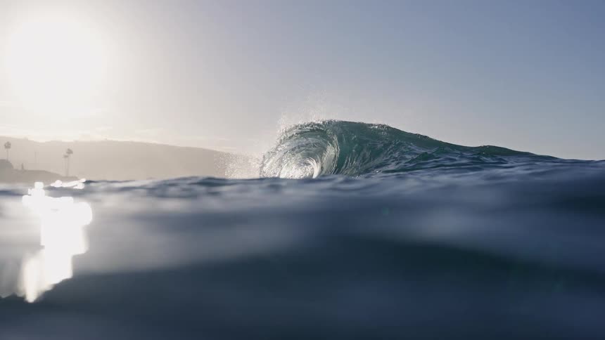 Slow motion half over half under water shot of a beautiful ocean wave barreling as the sun shines brightly
