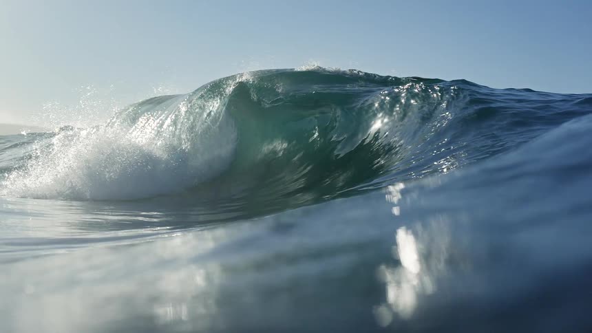 Dramatic slow-motion shot from water level of a powerful ocean wave cresting and breaking under a clear sky