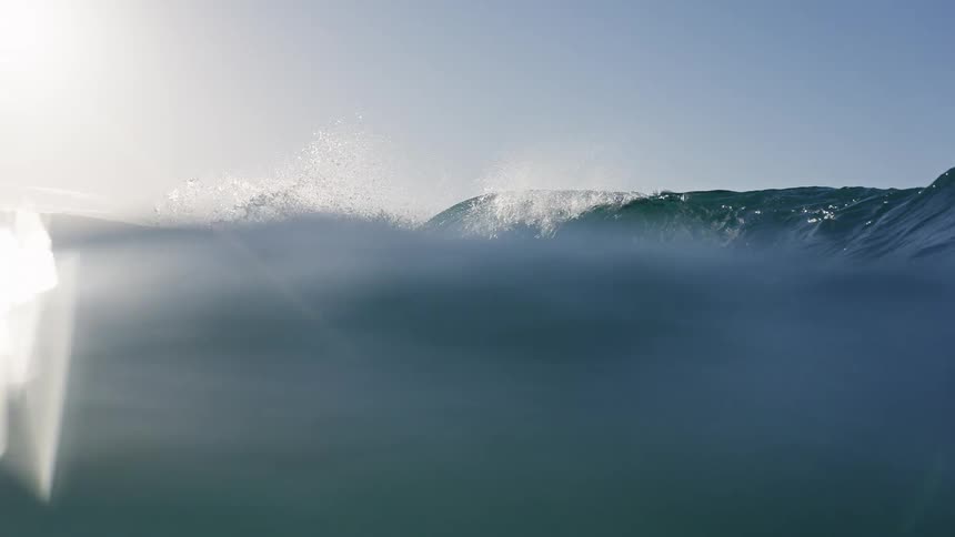 An immersive slow-motion view of a majestic ocean wave curling and breaking, filmed from the water's surface