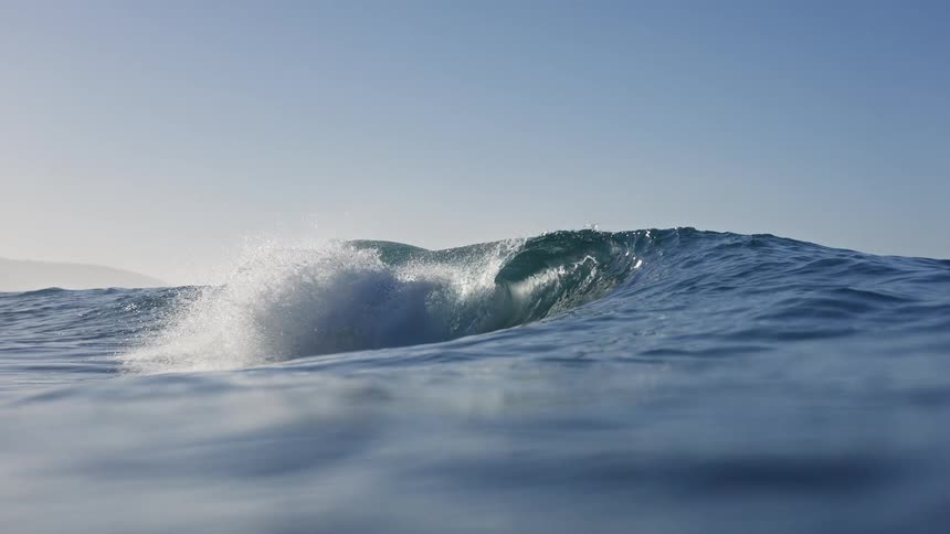 A majestic ocean wave builds and breaks in beautiful slow motion from a water-level perspective before submerging the camera
