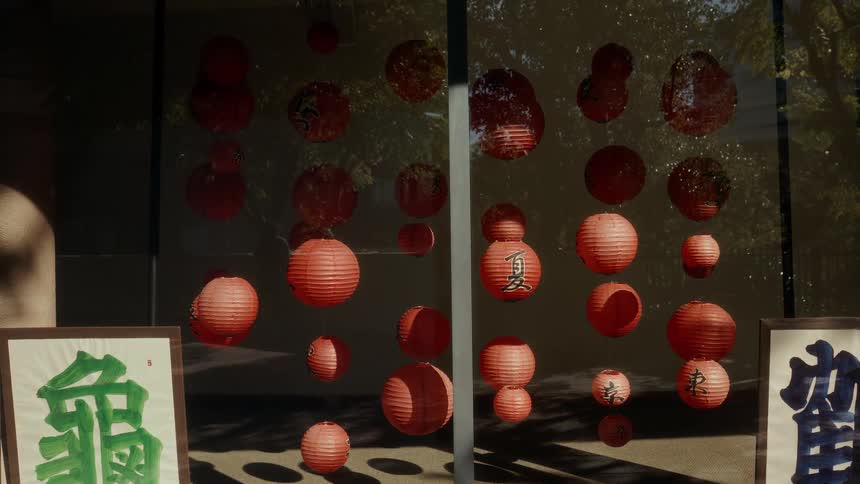 Sunlight illuminates a collection of red Japanese paper lanterns and calligraphy art hanging in a tranquil window display