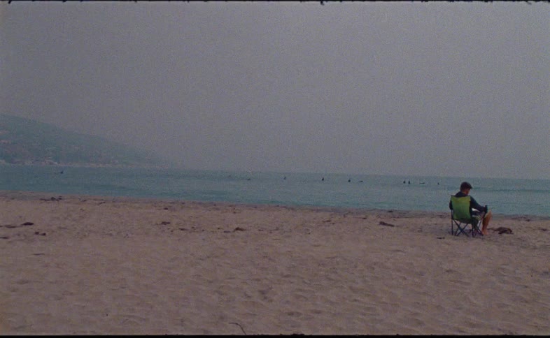 A solitary man sits in a beach chair watching the ocean on a foggy day in this grainy vintage footage