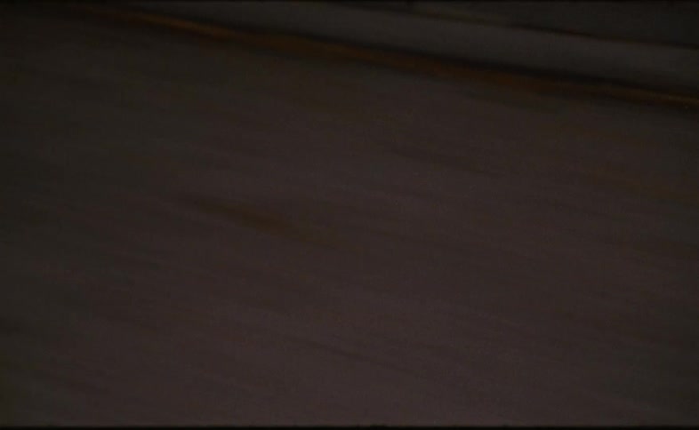 An abstract, grainy point-of-view shot from a moving vehicle looking down at the road speeding by at night