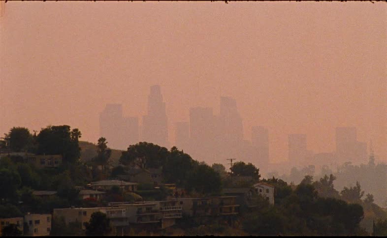 A grainy, vintage shot captures the hazy, orange-tinted skyline of Los Angeles obscured by heavy smog