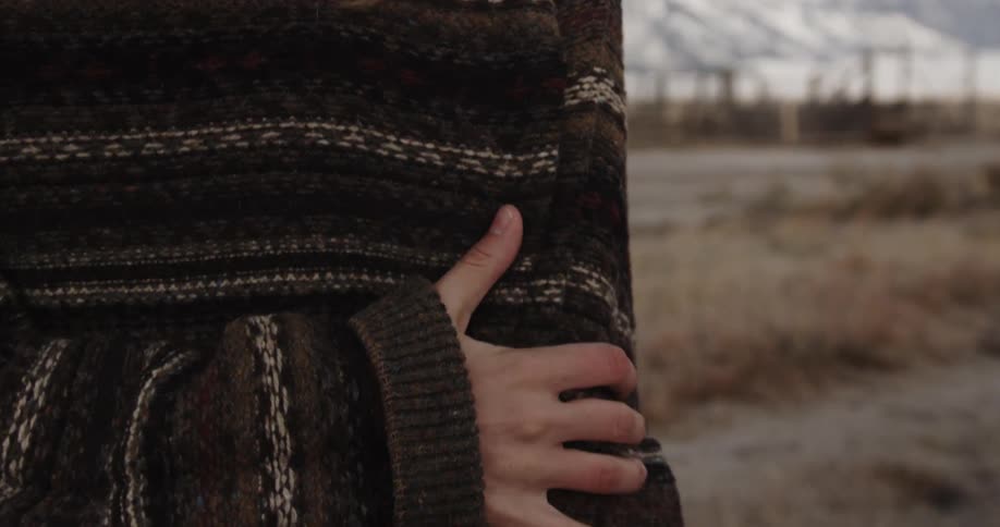 A woman rubs her arm while wearing a sweater outside