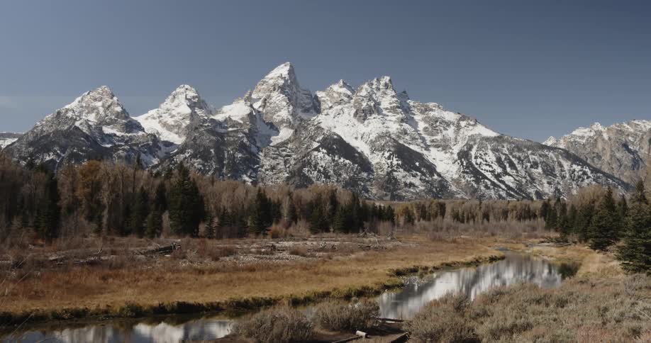 A lake sits in front of snowy mountains on a sunny day