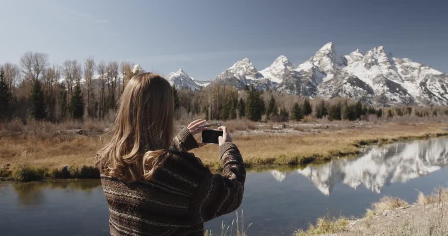 A woman takes a picture of a mountain lake