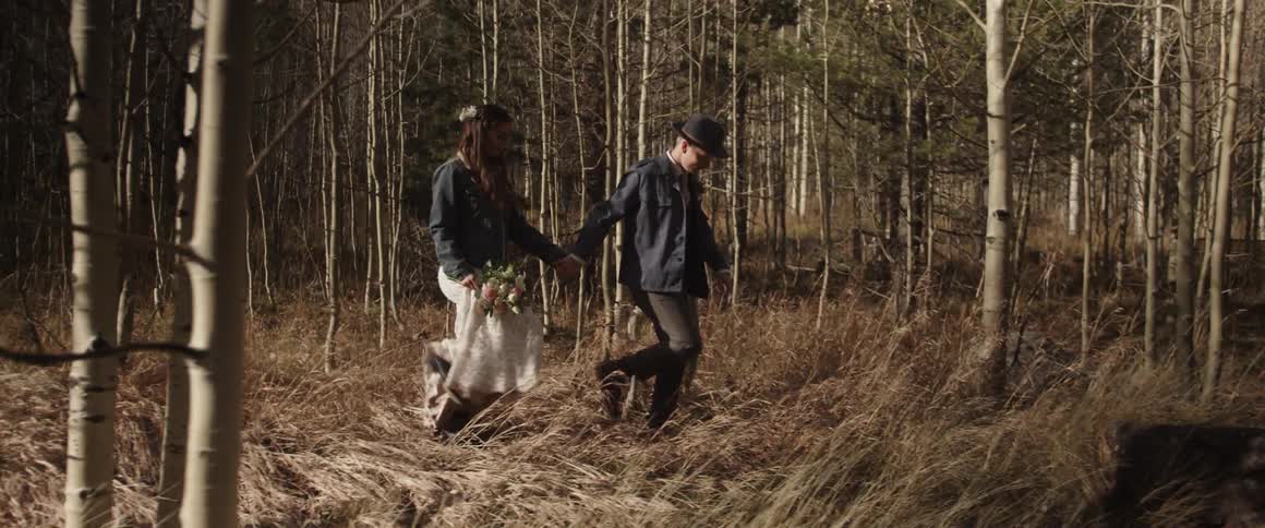 A bride and groom hold hands while walking in the woods