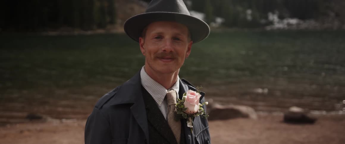 A man smiles while standing by a lake