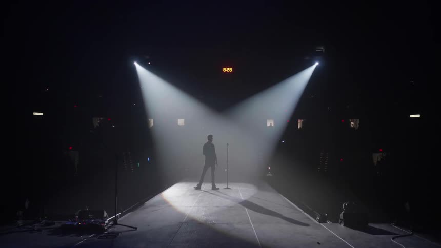 A man walks around stage under a spotlight
