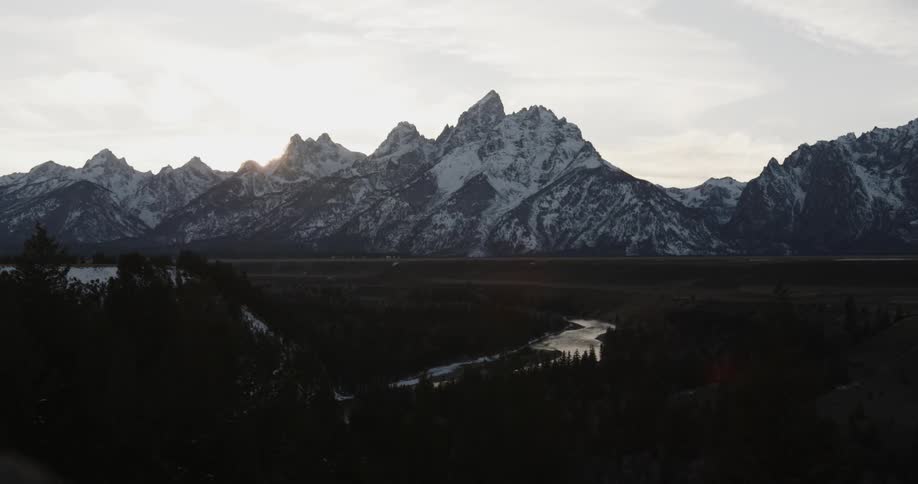 The sun is setting beyond snow covered mountains
