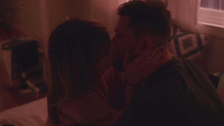 Man and woman sit on a bed kissing