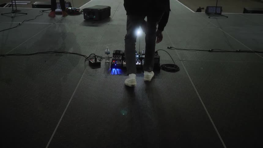 A man crouches down to adjust music equipment on a stage