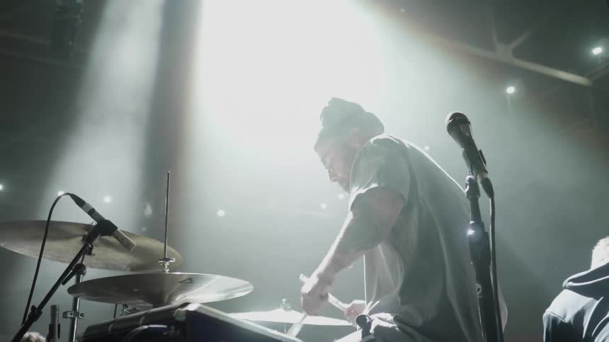 A man sits down and plays drums on stage