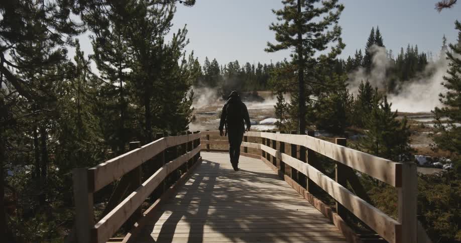 A man walks on a wood walkway towards hot springs