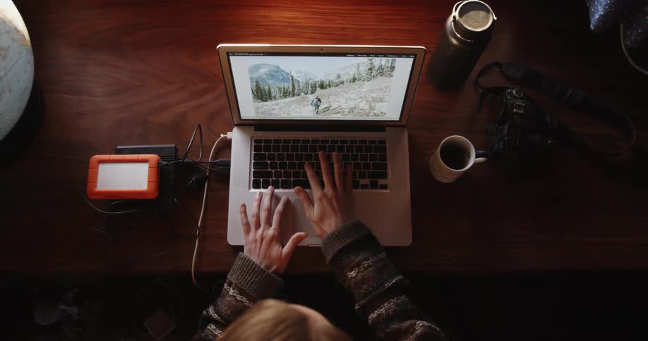 A woman looks at photographs on a laptop and drinks from a mug