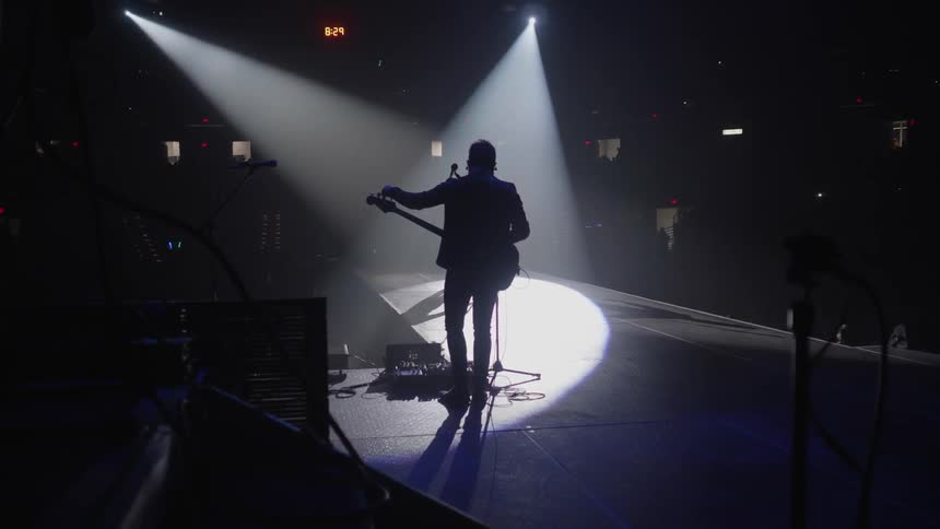A man adjusts his guitar while standing in the spotlight