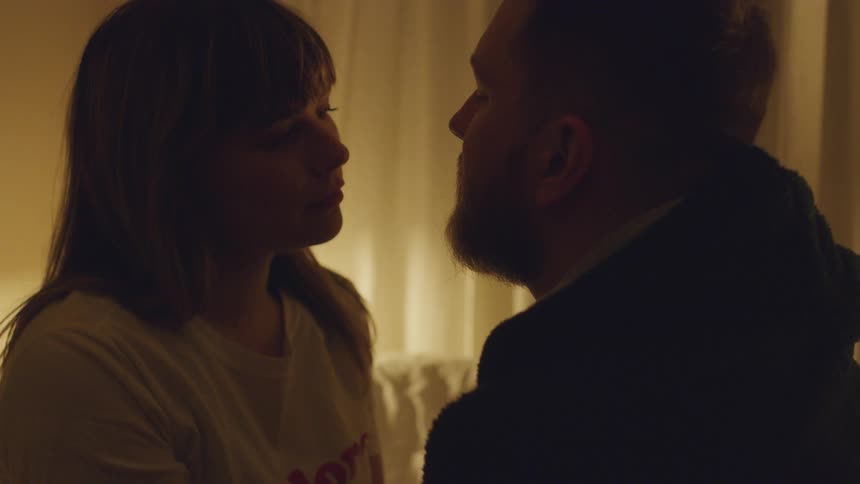 A man and woman talk in a dimly lit room