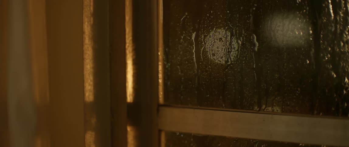 Rain drizzles down a window at night