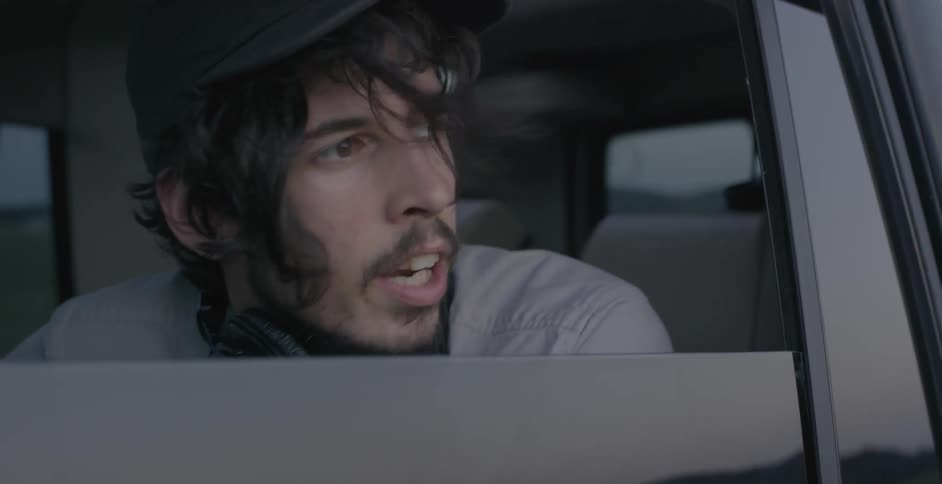 A man sitting inside a car with headphones around his neck and talking out the window