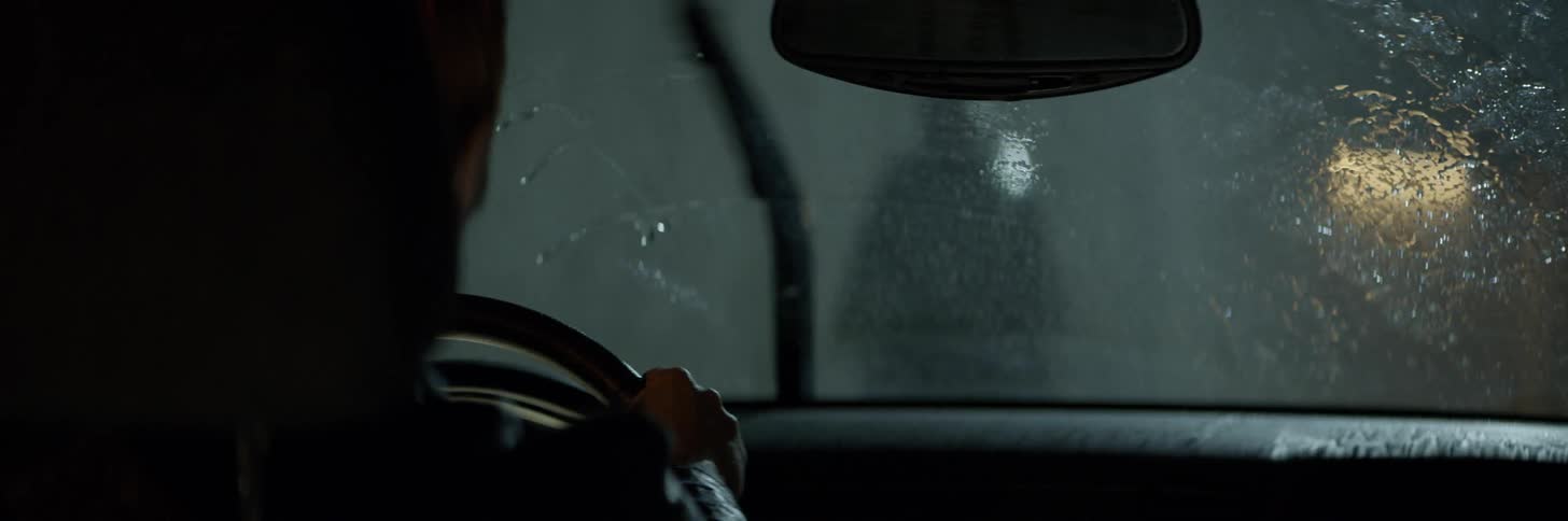 Rain falls on a car blocked by a man in a rain poncho