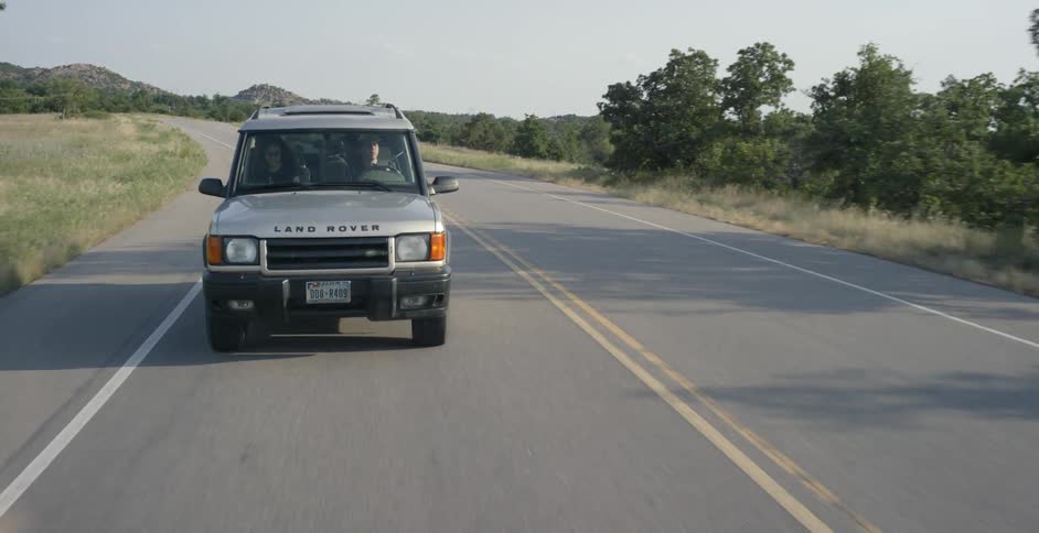 A gray land rover travels down a road during the day