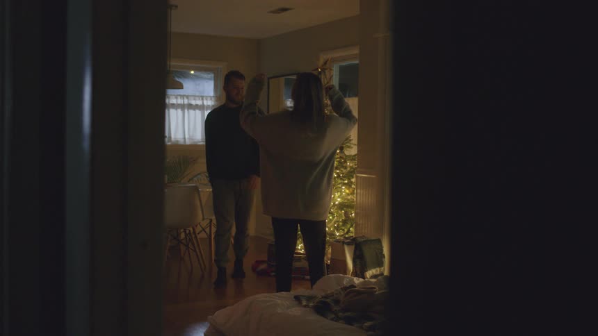 A woman watches her husband plug in a christmas tree