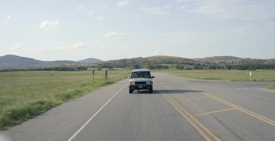 A gray land rover travels down an empty road