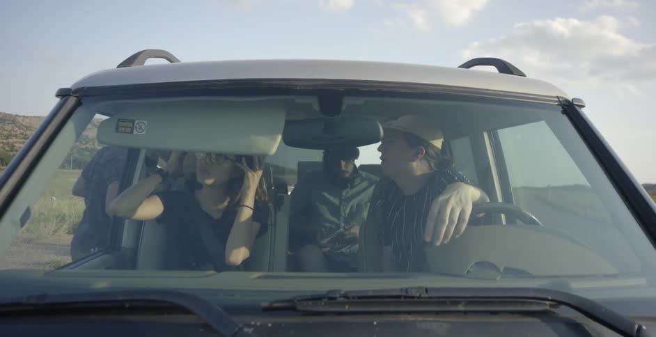 A woman and two men sit in a parked jeep as another man gets in
