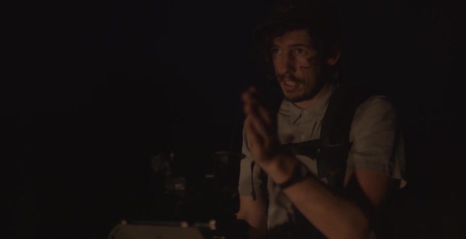 Man carrying camera equipment waves his arm